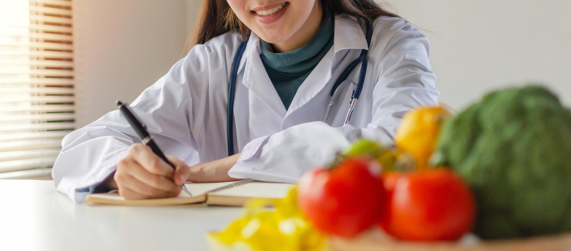 A nutritionist writing notes beside fresh vegetables