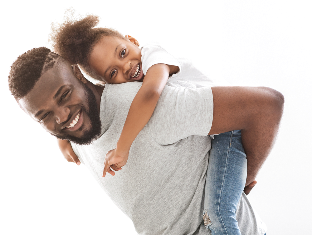 A father gives his young child a piggyback ride, both smiling.