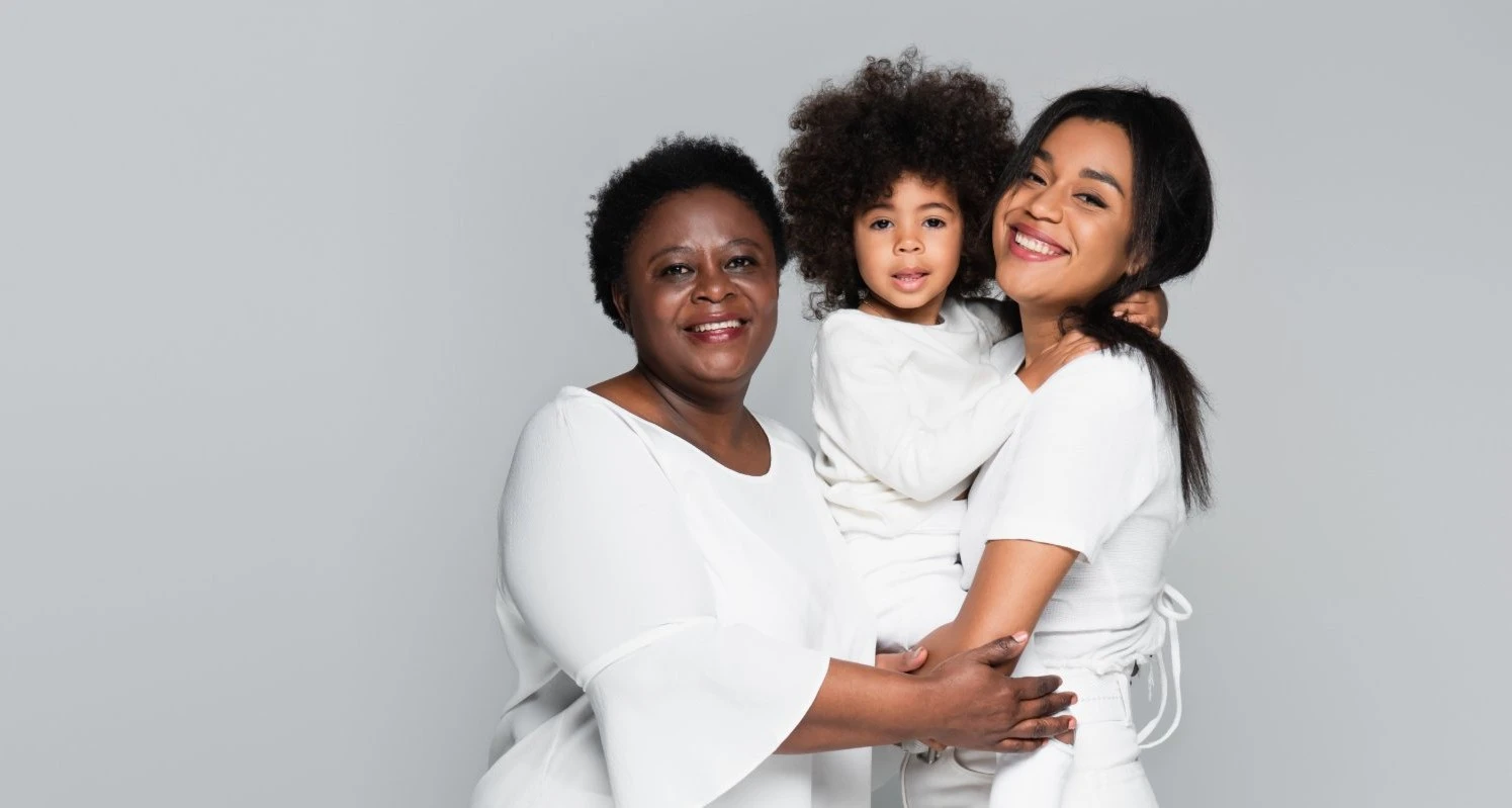 A grandmother, mother and young child smile together in white clothing