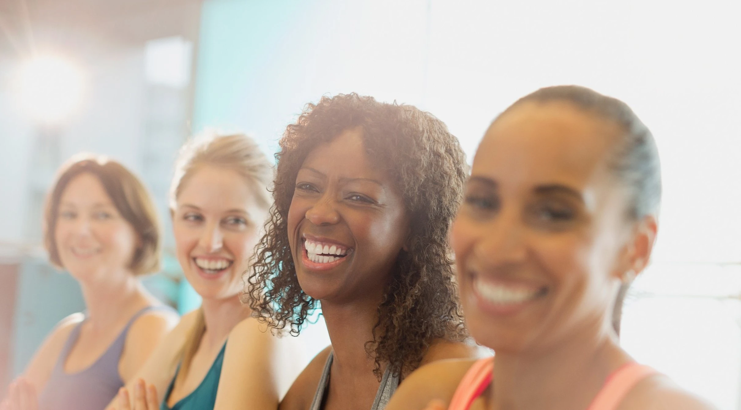 Four women laugh together in a bright fitness class